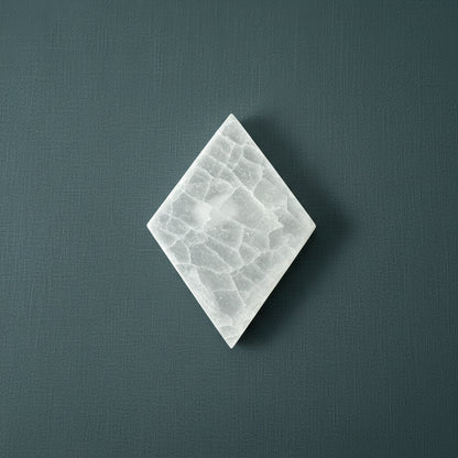 A diamond-shaped selenite slice with a soft translucent texture displayed upright on a muted dark textured background. — for Carpe Diem Dream