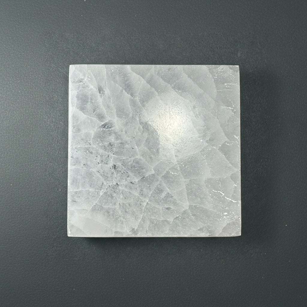 A square selenite slice with a soft translucent texture displayed upright on a muted dark textured background. — for Carpe Diem Dream