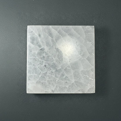 A square selenite slice with a soft translucent texture displayed upright on a muted dark textured background. — for Carpe Diem Dream