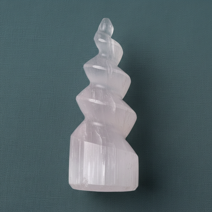 A close-up view of a carved selenite spiral tower showing its smooth translucent layers against a muted teal background. — for Carpe Diem Dream