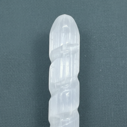 A close-up view of a translucent white selenite spiral wand showcasing its carved tip and natural striations. — for Carpe Diem Dream