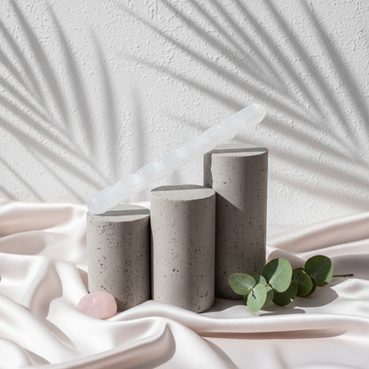 A translucent white selenite spiral wand resting diagonally across neutral stone pedestals with soft botanical shadows. — for Carpe Diem Dream