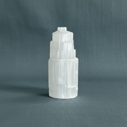 A translucent white selenite standing tower displayed upright on a muted sage linen background. — for Carpe Diem Dream