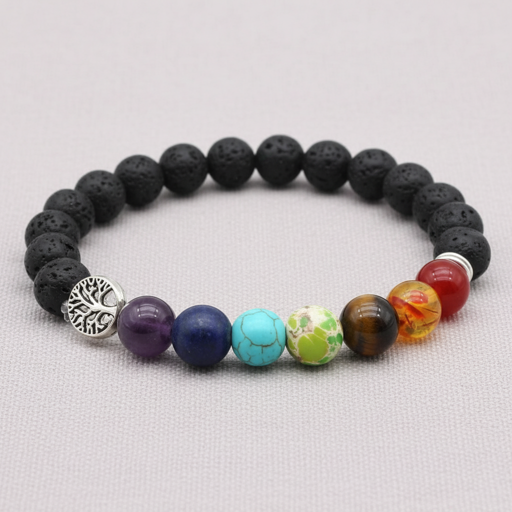 A close-up of a black lava stone stretch bracelet with multicolored chakra beads and a silver Tree of Life charm displayed on a light fabric background. — for Carpe Diem Dream
