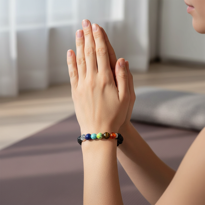 A person wearing a black lava stone chakra bracelet with multicolored beads and a silver Tree of Life charm while sitting indoors with hands in a prayer position. — for Carpe Diem Dream