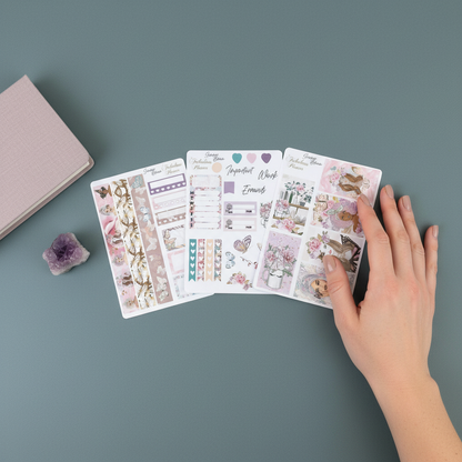 Hand placed beside three Miss Butterfly 4x6 planner sticker sheets on a muted teal surface with a notebook and amethyst crystal. — for Carpe Diem Dream