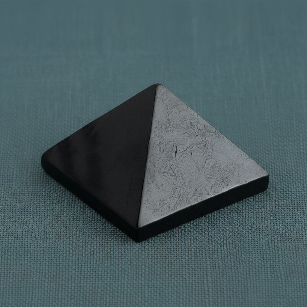 Black shungite pyramid displayed upright on a muted teal linen surface with soft diffused lighting and subtle shadow. — for Carpe Diem Dream