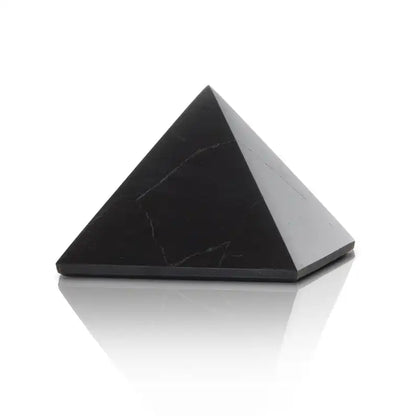 Black shungite pyramid displayed on a clean white background with subtle reflection, showing natural stone texture and shape. — for Carpe Diem Dream
