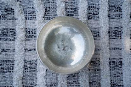 Close-up top view of a silver Tibetan singing bowl showing the hammered interior surface resting on a textured woven cloth background. — for Carpe Diem Dream