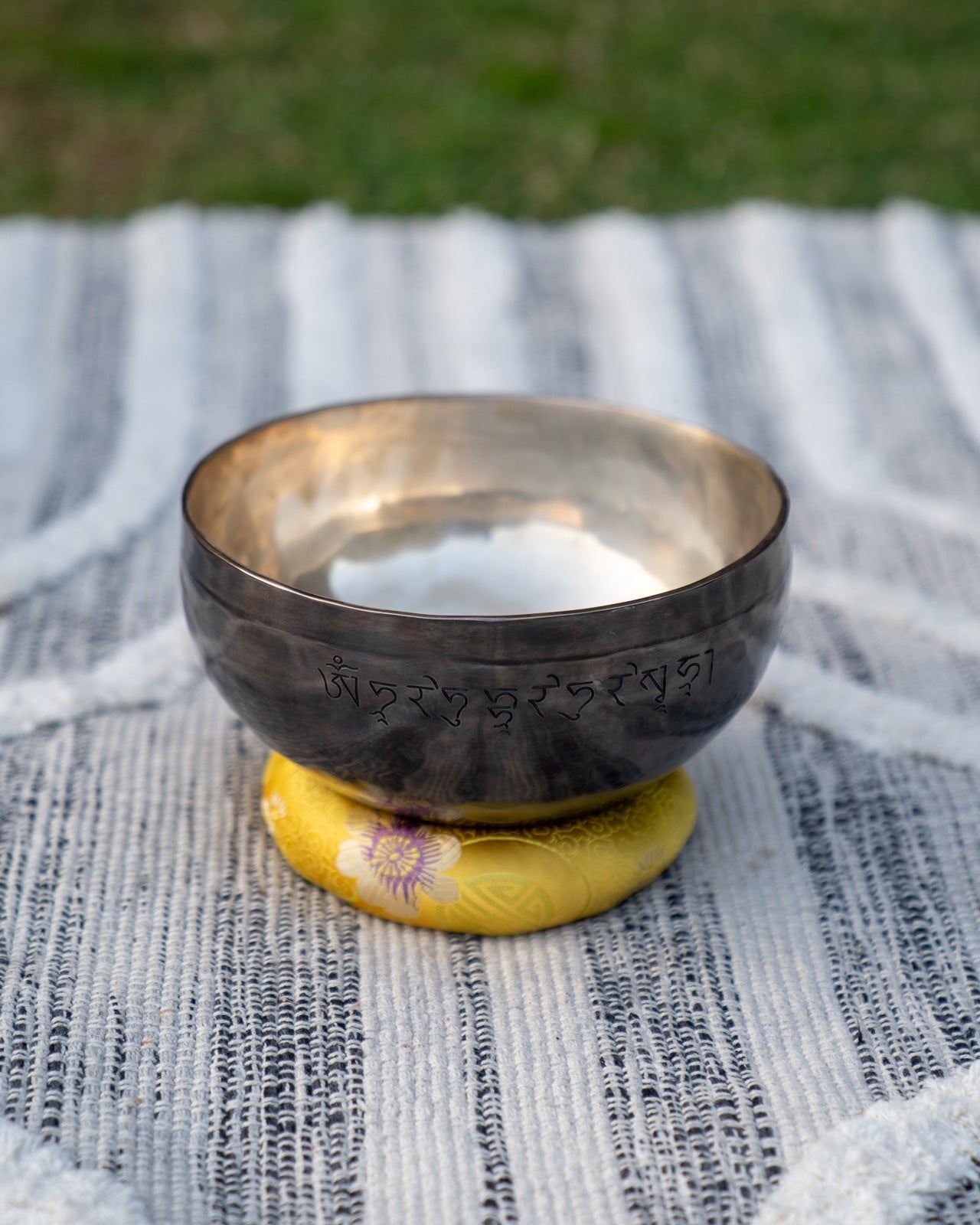 Back view of a Solar Plexus Chakra New Moon singing bowl showing engraved Tibetan mantra resting on a yellow cushion. — for Carpe Diem Dream