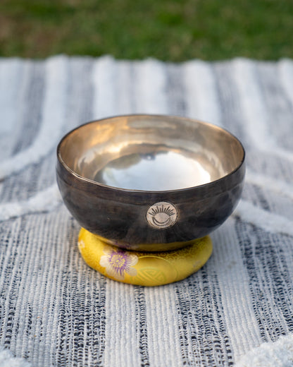 Front view of a Solar Plexus Chakra New Moon singing bowl with engraved sun and moon symbol resting on a yellow cushion. — for Carpe Diem Dream
