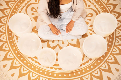 Top view of six white frosted crystal singing bowls arranged in a circle on a patterned rug with a seated woman — for Carpe Diem Dream