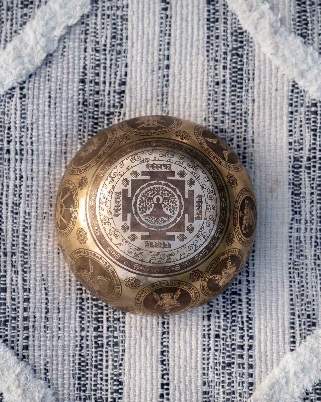 Bottom view of carved Tibetan singing bowl showing Buddha meditating within a mandala engraving on textured blue and white linen fabric. — for Carpe Diem Dream
