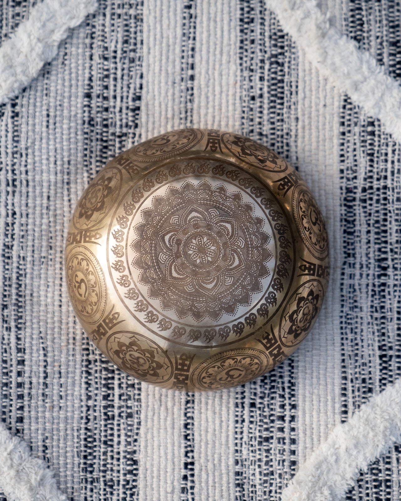 Bottom view of carved Tibetan singing bowl showing lotus mandala engraving on textured blue and white linen fabric. — for Carpe Diem Dream