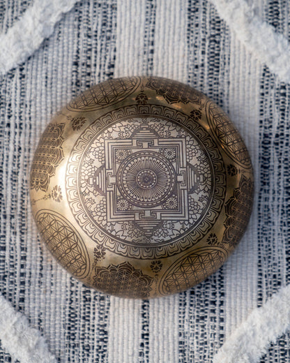 Bottom view of carved Tibetan singing bowl showing intricate mandala engraving on textured blue and white linen fabric. — for Carpe Diem Dream