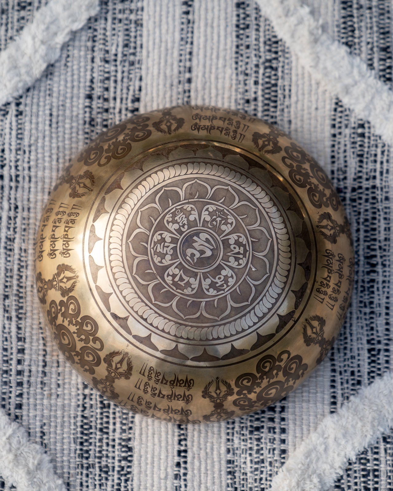 Bottom view of carved Tibetan singing bowl showing Om symbol within an intricate mandala engraving on textured blue and white linen fabric. — for Carpe Diem Dream