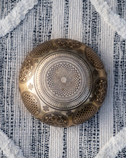 Bottom view of carved Tibetan singing bowl showing radial mandala geometric engraving on textured blue and white linen fabric. — for Carpe Diem Dream
