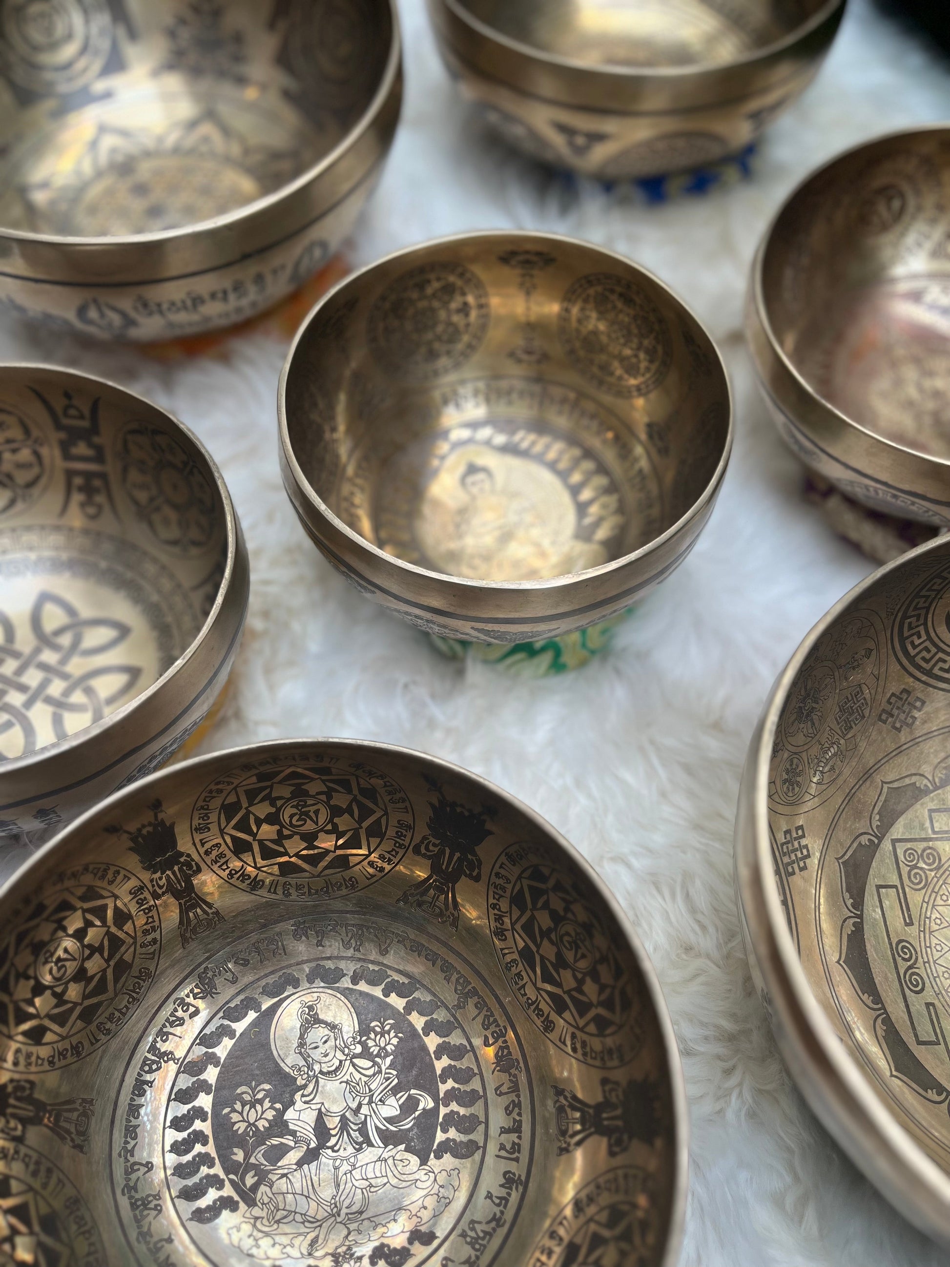 Close-up view of carved Tibetan singing bowls showing intricate mandala and Sanskrit designs on a textured white fur surface. — for Carpe Diem Dream