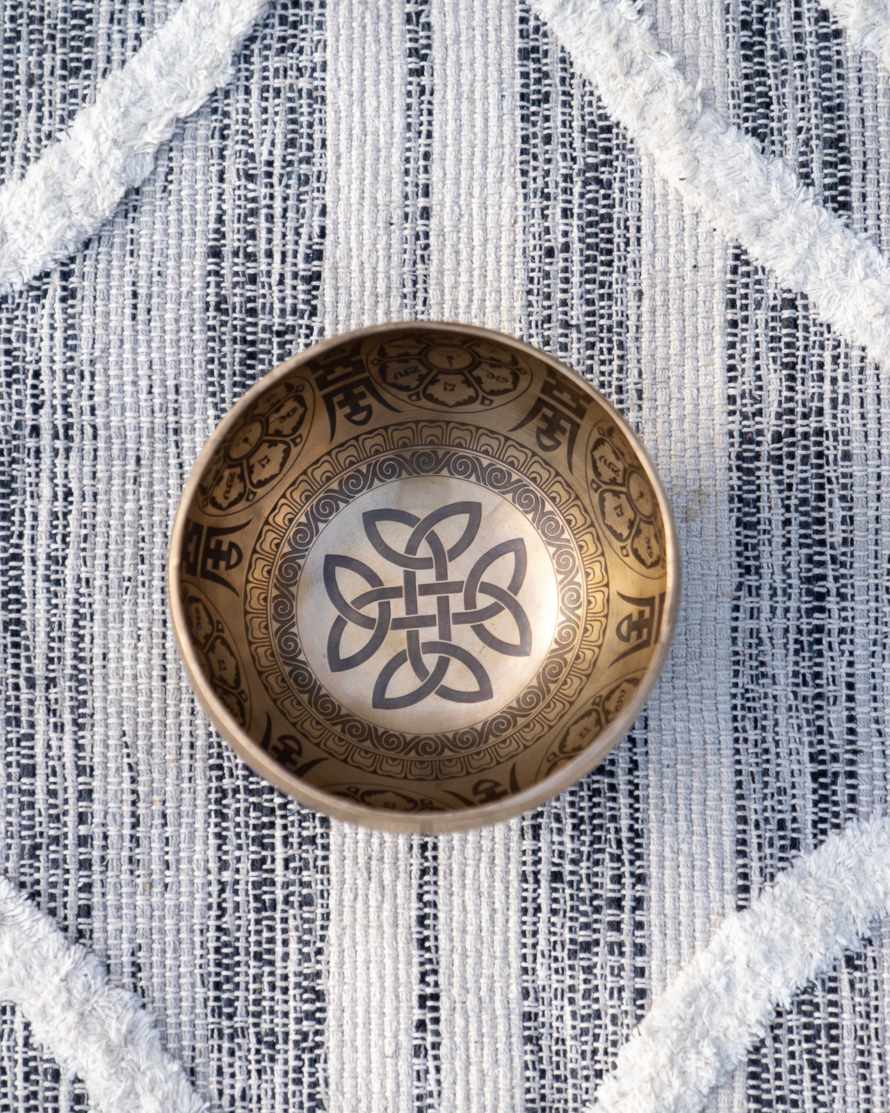 Top view of carved Tibetan singing bowl showing endless knot Buddhist symbol engraved inside the bowl on textured blue and white linen fabric. — for Carpe Diem Dream
