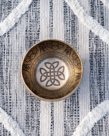 Top view of carved Tibetan singing bowl showing endless knot Buddhist symbol engraved inside the bowl on textured blue and white linen fabric. — for Carpe Diem Dream