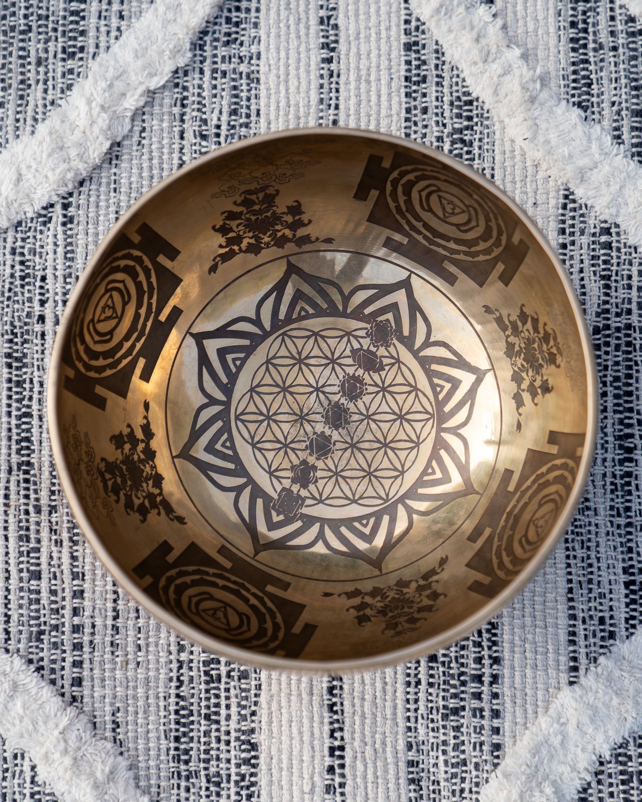Top view of carved Tibetan singing bowl showing Flower of Life sacred geometry and lotus mandala engraving on textured blue and white linen fabric. — for Carpe Diem Dream