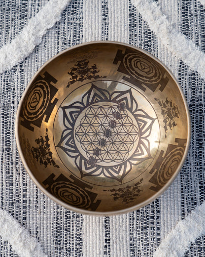 Top view of carved Tibetan singing bowl showing Flower of Life sacred geometry and lotus mandala engraving on textured blue and white linen fabric. — for Carpe Diem Dream