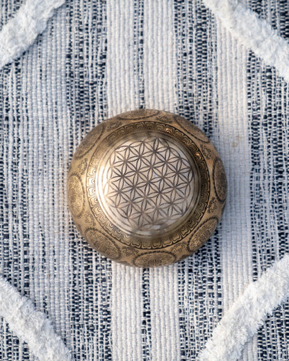 Top view of carved Tibetan singing bowl showing Flower of Life sacred geometry pattern engraved in the center on textured blue and white linen fabric. — for Carpe Diem Dream