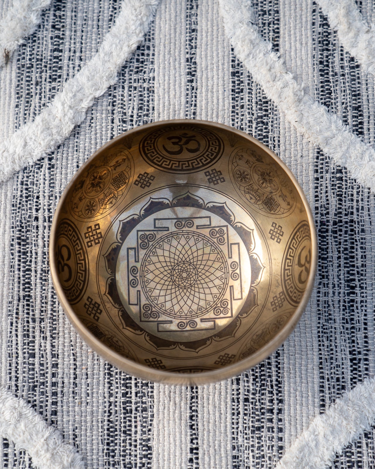 Top view of carved Tibetan singing bowl showing Sri Yantra sacred geometry and Om symbols engraved inside the bowl on textured blue and white linen fabric. — for Carpe Diem Dream