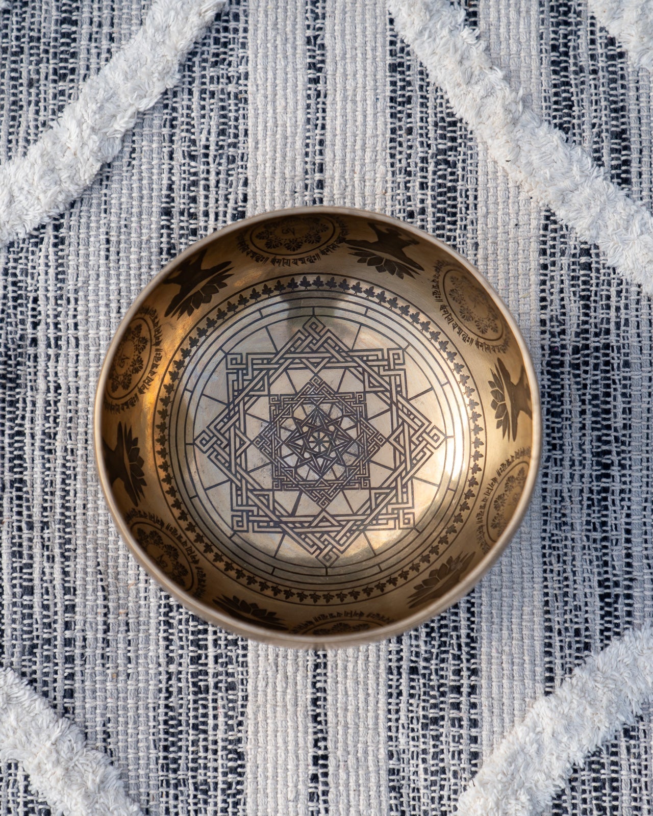 Top view of carved Tibetan singing bowl showing star mandala sacred geometry and Om symbols engraved inside the bowl on textured blue and white linen fabric. — for Carpe Diem Dream