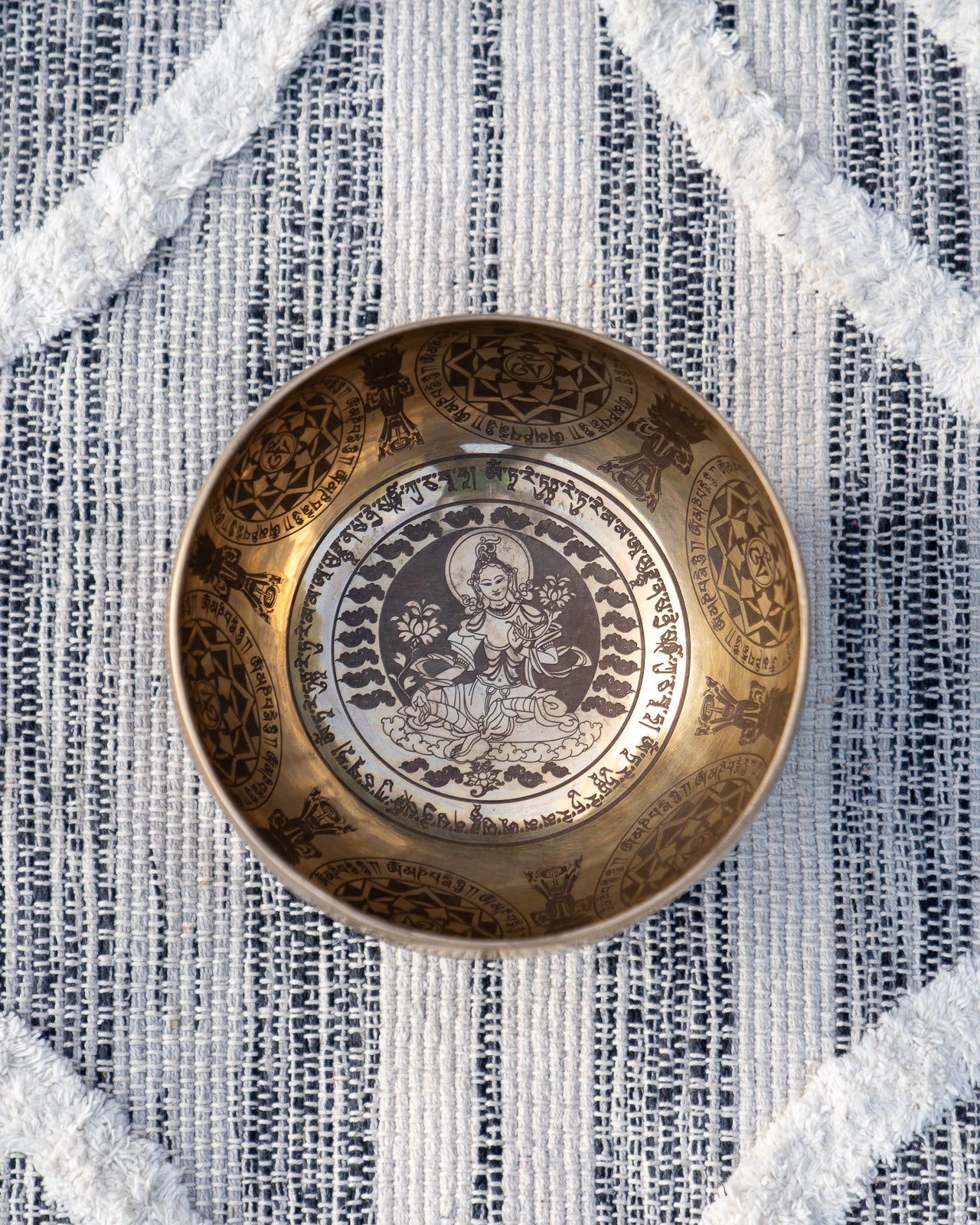 Top view of carved Tibetan singing bowl featuring Tara deity engraving surrounded by mantra script on textured blue and white linen fabric. — for Carpe Diem Dream