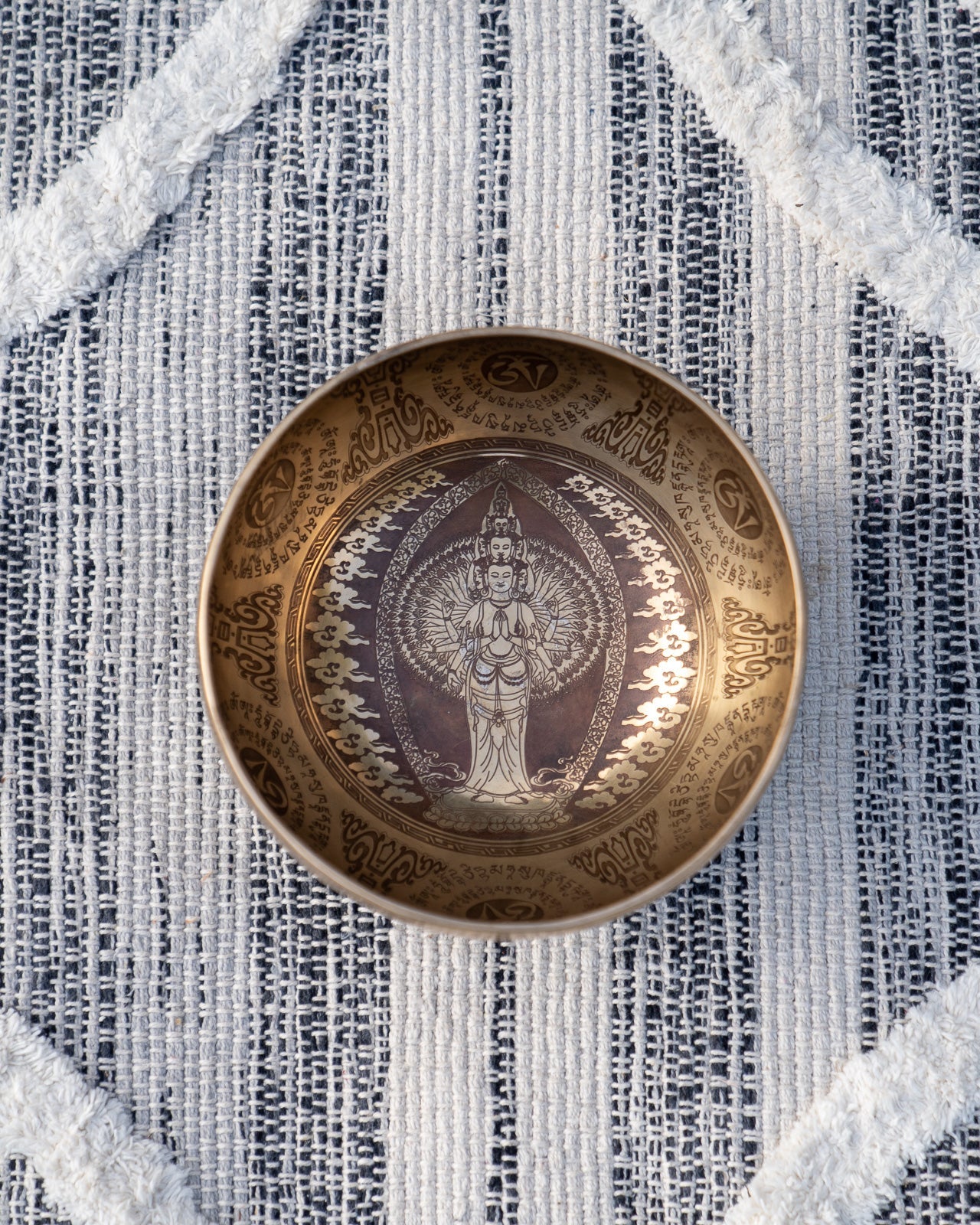 Top view of carved Tibetan singing bowl featuring standing Tara deity engraving surrounded by mantra script on textured blue and white linen fabric. — for Carpe Diem Dream