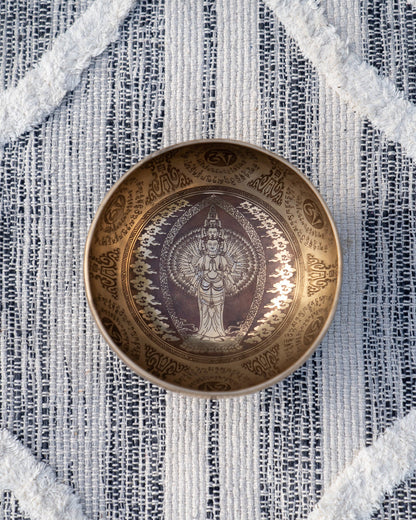 Top view of carved Tibetan singing bowl featuring standing Tara deity engraving surrounded by mantra script on textured blue and white linen fabric. — for Carpe Diem Dream