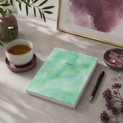 Start Anytime Undated 52-Week Planner paperback by Big Fish Planners displayed on a cool limestone workspace with a cup of tea, writing pen, mauve accents, and soft natural daylight, illustrating intentional planning, productivity, goal setting, and organized living in a refined editorial lifestyle setting — for Carpe Diem Dream