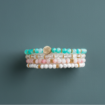 A stacked set of four crystal bead bracelets featuring Amazonite, Pink Opal, Clear Quartz, and Howlite displayed on a muted teal surface. — for Carpe Diem Dream