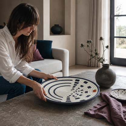 Large Sunrise Wall Basket being gently placed on a stone table as part of a calm home styling moment with dark teal, mauve, and soft neutral accents. — for Carpe Diem Dream