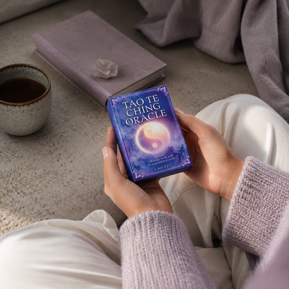 The Tao Te Ching Oracle Book & Cards held during a quiet moment of self-reflection with tea, soft mauve textiles, and cool diffused daylight in a calm sanctuary setting. — for Carpe Diem Dream