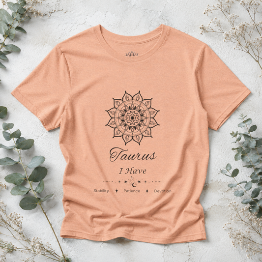 Taurus Sun I Have zodiac T-shirt in heather peach with black sun-inspired mandala artwork and Stability, Patience, Devotion text, styled in a cool-toned studio botanical flat lay. — for Carpe Diem Dream