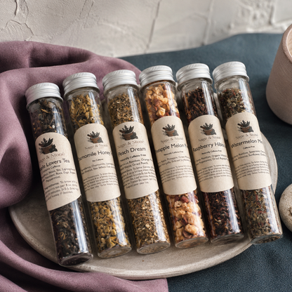Fruity Tea Sampler tubes displayed close-up on a stone tray with visible loose tea textures, cream labels, silver caps, mauve linen, and dark teal styling. — for Carpe Diem Dream