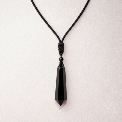 IBlack obsidian talisman necklace hanging against a soft pale pink textured background. — for Carpe Diem Dream