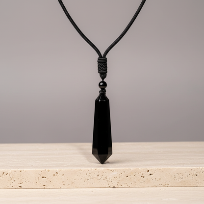 Black obsidian talisman necklace displayed on a travertine stone surface with soft neutral lighting. — for Carpe Diem Dream