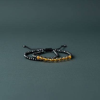 Mindfulness bracelet with glossy black hematite and warm citrine beads arranged on a muted teal matte surface with soft diffused lighting — for Carpe Diem Dream