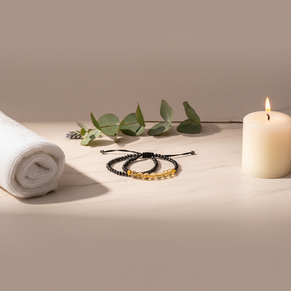 Mindfulness bracelet with glossy black hematite and warm citrine beads arranged beside a rolled white spa towel, eucalyptus sprigs, and a lit candle on a soft neutral surface — for Carpe Diem Dream