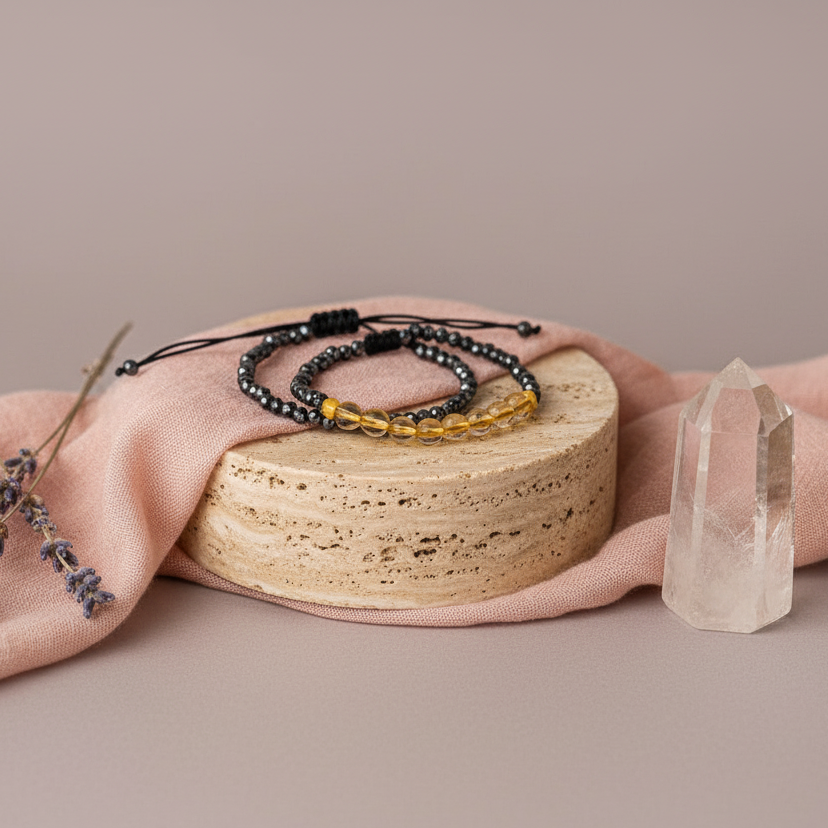 Mindfulness bracelet with glossy black hematite and warm citrine beads displayed on a round stone pedestal with soft mauve fabric, clear quartz, and lavender accents — for Carpe Diem Dream