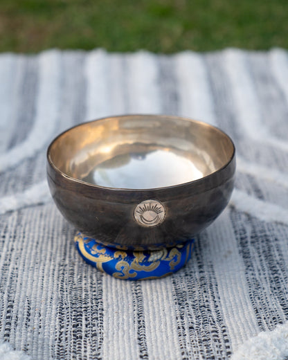 Third Eye Chakra New Moon singing bowl tuned to A note resting on a blue cushion on a textured woven cloth background. — for Carpe Diem Dream