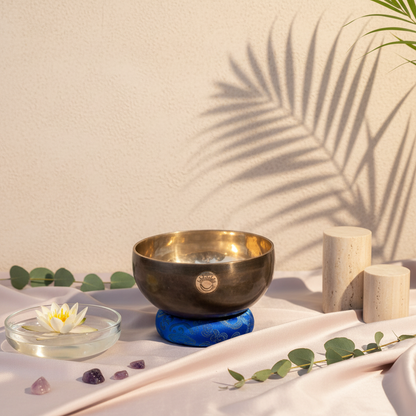 Hand-hammered Third Eye Chakra New Moon singing bowl tuned to A note resting on a blue cushion in a serene studio botanical scene with lotus flower, crystals, and soft botanical shadows. — for Carpe Diem Dream