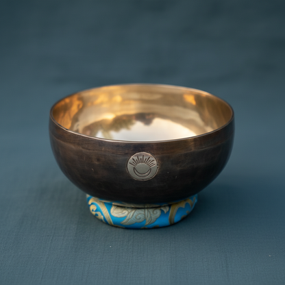 Close-up view of a hand-hammered Throat Chakra New Moon singing bowl tuned to G note showing the engraved symbol and bronze metal finish. — for Carpe Diem Dream