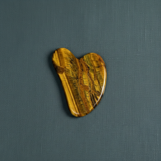 A tiger’s eye gua sha facial tool displayed on a textured muted teal linen surface with soft natural lighting. — for Carpe Diem Dream