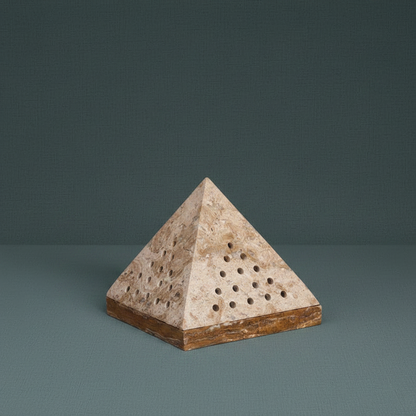 A beige travertine pyramid incense holder with perforated sides resting on a muted teal surface under soft natural light. — for Carpe Diem Dream