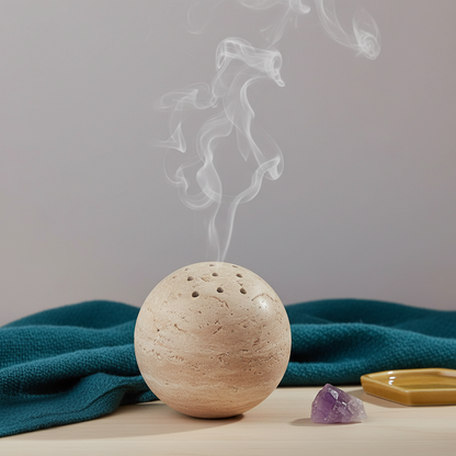 A travertine sphere incense burner releasing soft smoke on a neutral surface with teal fabric and small crystals in a calm meditation setting. — for Carpe Diem Dream