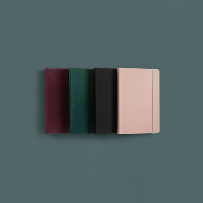 Four velvet hard cover journals in maroon, forest green, black, and blush pink displayed upright on a muted teal background. — for Carpe Diem Dream